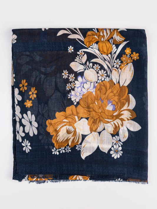 A square scarf with a dark navy blue base, featuring a large floral print in mustard yellow, white, and light blue, finished with fringed edges.
